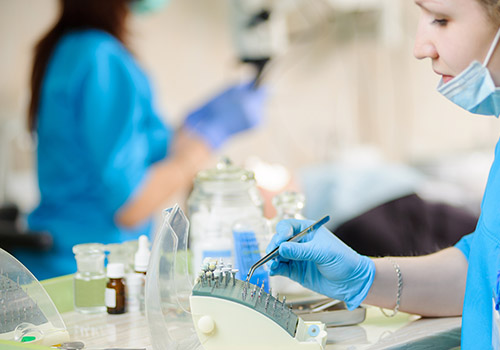 Close-up portrait of young female dentist assistant holding dental drill on foreground. Doctor working with microscope in the background. Dental equipment. Teeth care and tooth health